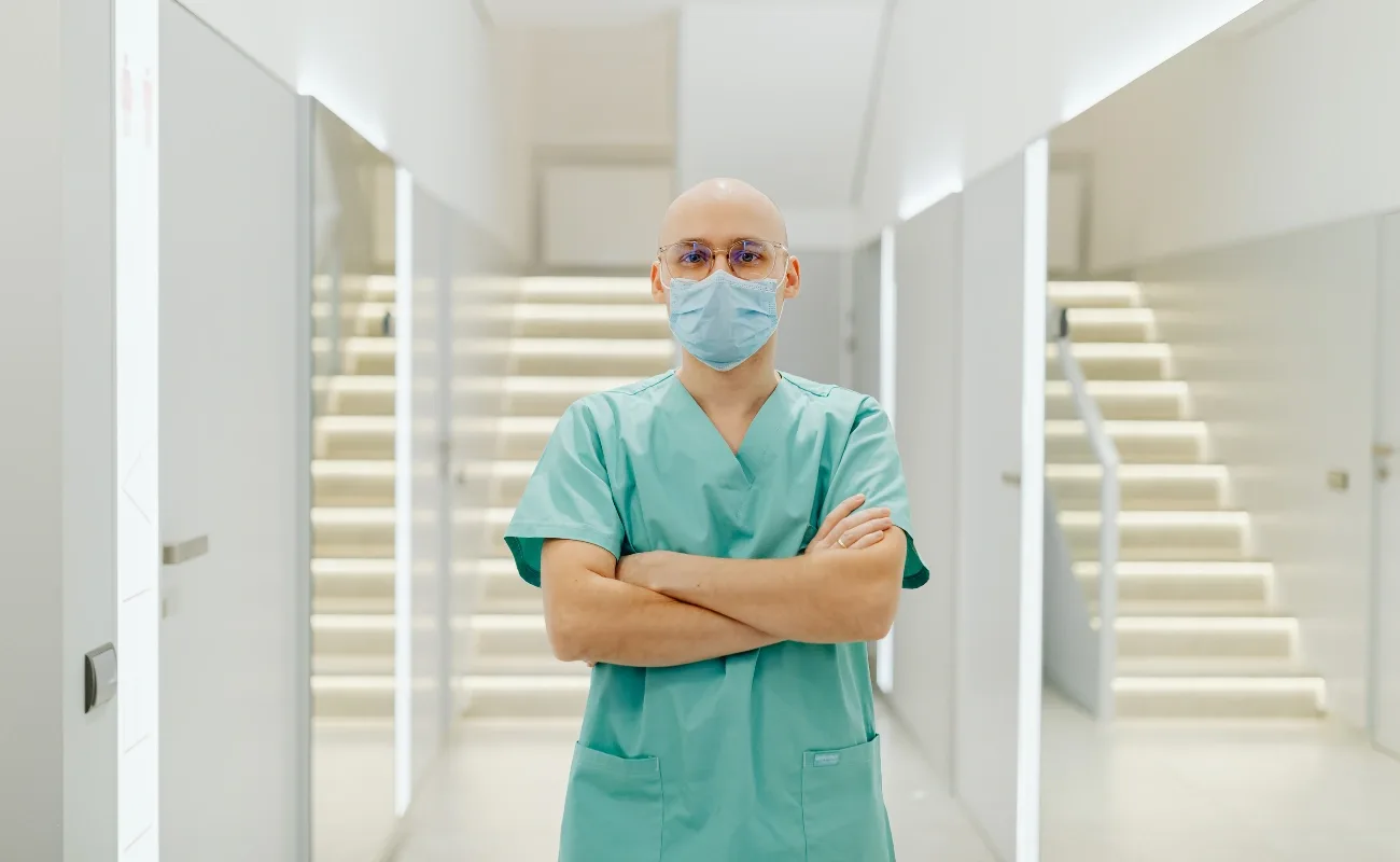 primary care physician in clinic hallway wearing scrubs and mask